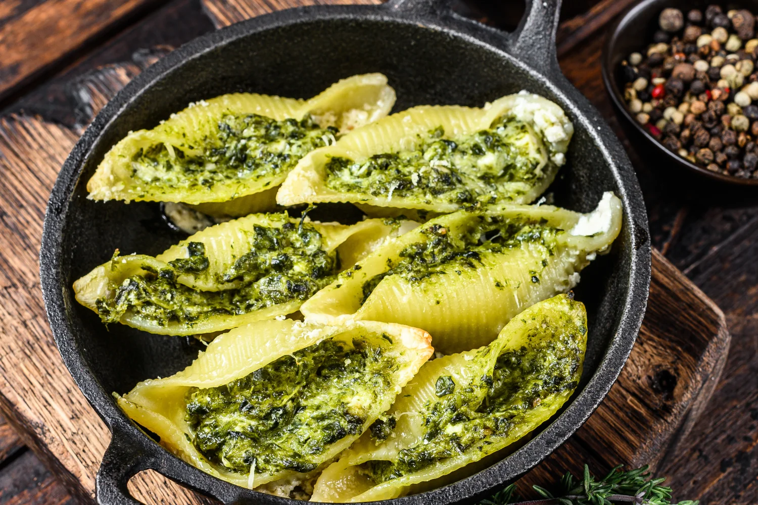 A bowl of large conchiglioni pasta shells coated in a vivid green blended pesto and spinach sauce, topped with freshly grated Parmesan and toasted pine nuts