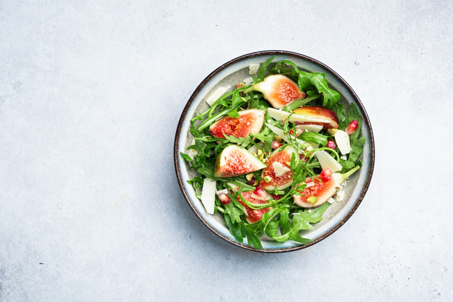 A serving platter of rocket leaves topped with quartered fresh figs, shaved Parmesan, crushed pistachios and pomegranate seeds, drizzled with a raspberry vinaigrette