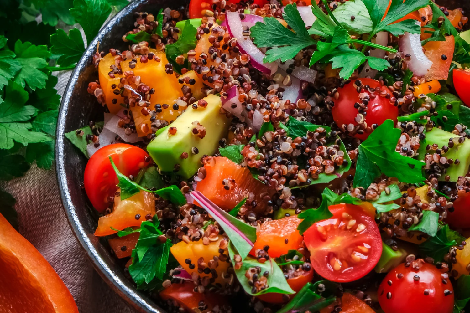 A large bowl of Mediterranean quinoa salad with diced avocado, cherry tomatoes, yellow pepper, red onion and fresh parsley, dressed with lemon and olive oil